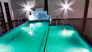 Una piscina con agua cristalina, un borde de baldosas y dos luces brillantes a cada lado.