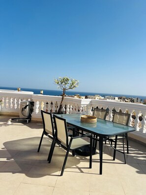 A terrace with a table and chairs, a small tree, and a view of the sea.