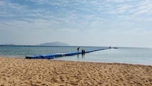 Uma praia com um longo pier que se estende para a água, c éu claro e montanhas ao longe.
