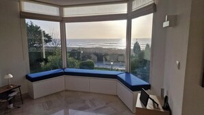 Habitación de esquina con ventanal que da al mar, un pequeño escritorio con una silla y una lámpara.