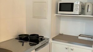 A compact kitchen with a stove, microwave, and kettle on a white countertop.