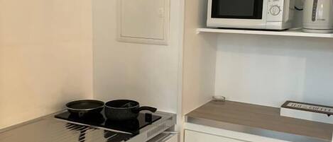 Cocina compacta con estufa, microondas y hervidor sobre una encimera blanca.