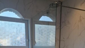 A bathroom with a marble wall, a bathtub, a shower area, and a window with a city view.