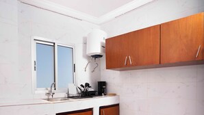 A kitchen with white marble tiles, wooden cabinets, a window, and a built-in stove. - Residence Hotel Edouard (Abidjan)