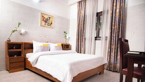 A neatly arranged bedroom with a wooden bed, bedside tables, a desk, and a chair. - Residence Hotel Edouard (Abidjan)