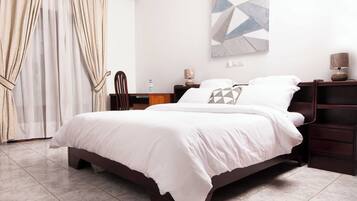 A hotel room with a large bed, a desk, a chair, a nightstand, a lamp, and a painting on the wall.