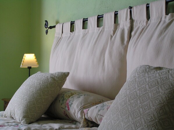 Una cama con cabecera, almohadas y una lámpara de noche.