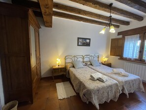 A bedroom with two beds, wooden beams, a white radiator, and a window with a curtain.