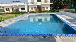 Et rektangulært swimmingpool med blå mosaikfliser langs kanten, omgivet af en skakmønstret fliseterrasse.