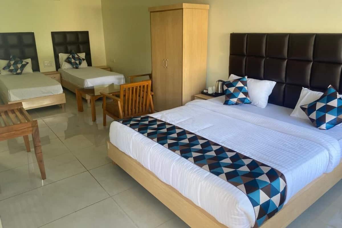 A hotel room with a large bed, two smaller beds, a wooden wardrobe, a desk, and a chair.