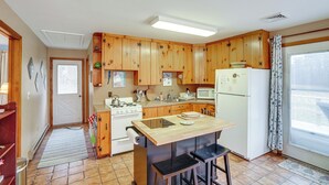 A kitchen with wooden cabinets, a stove, a microwave, and a refrigerator. There is a window with a curtain and a door leading to another room.