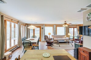 A spacious living room with a dining area, large windows, and a ceiling fan.