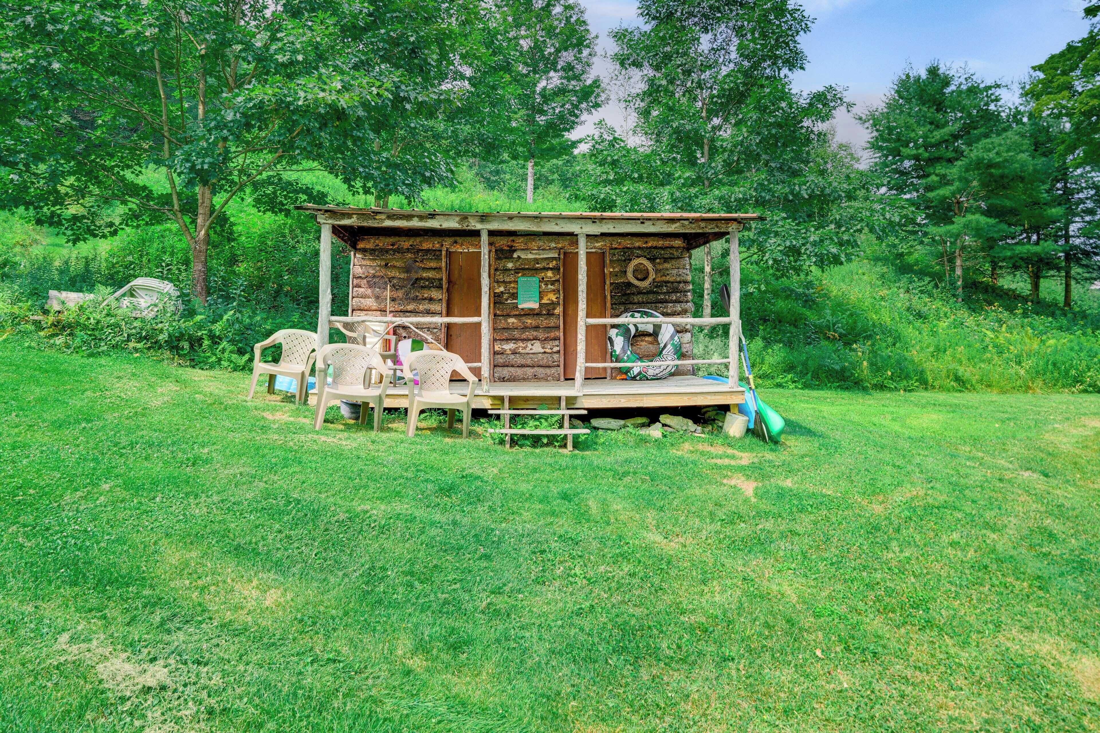 A rustic wooden cabin with a porch, surrounded by lush greenery.