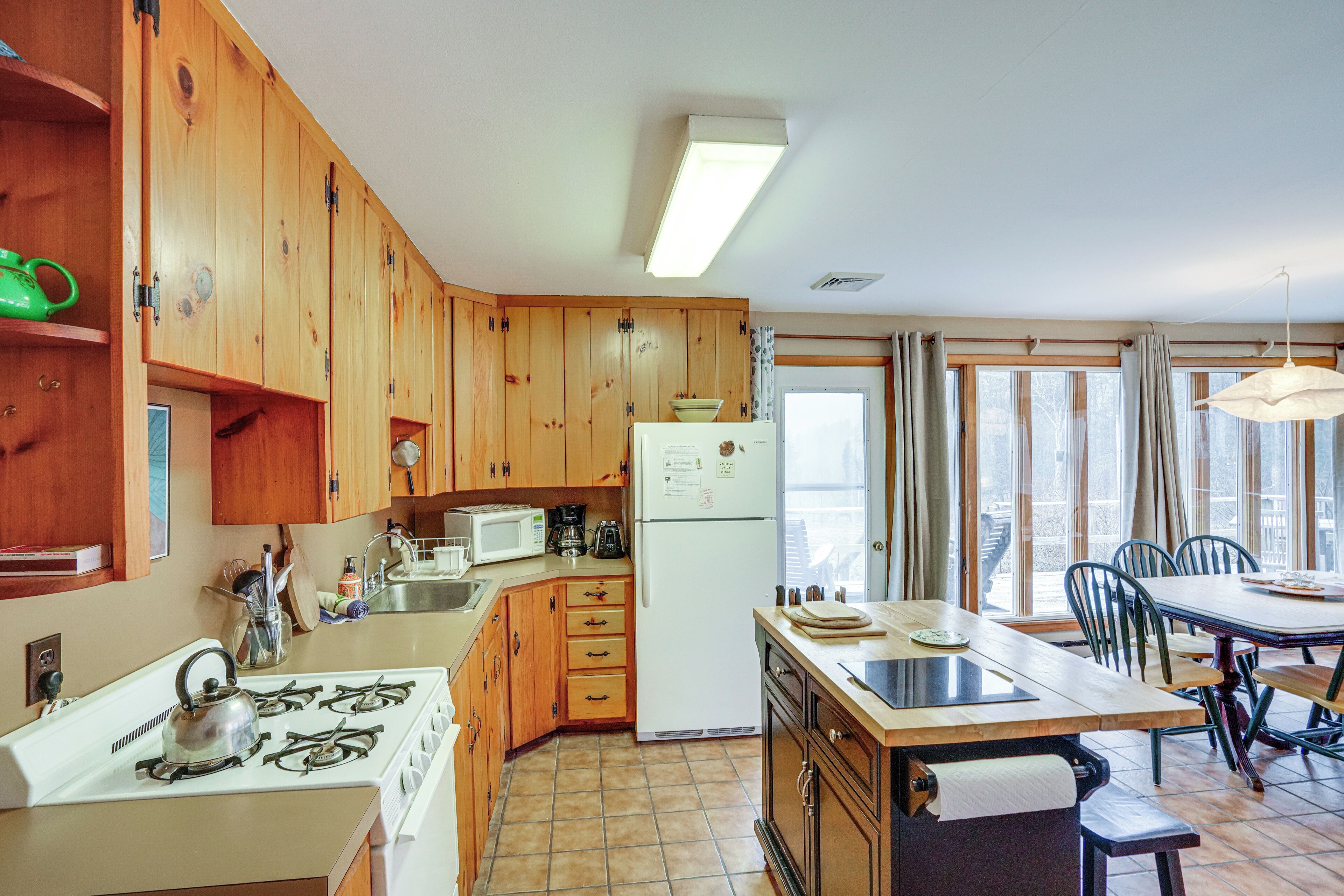 A kitchen with wooden cabinets, a stove, a refrigerator, and a dining area with chairs and a table.
