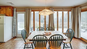 A dining area with a table and chairs, large windows, and a hanging light fixture.