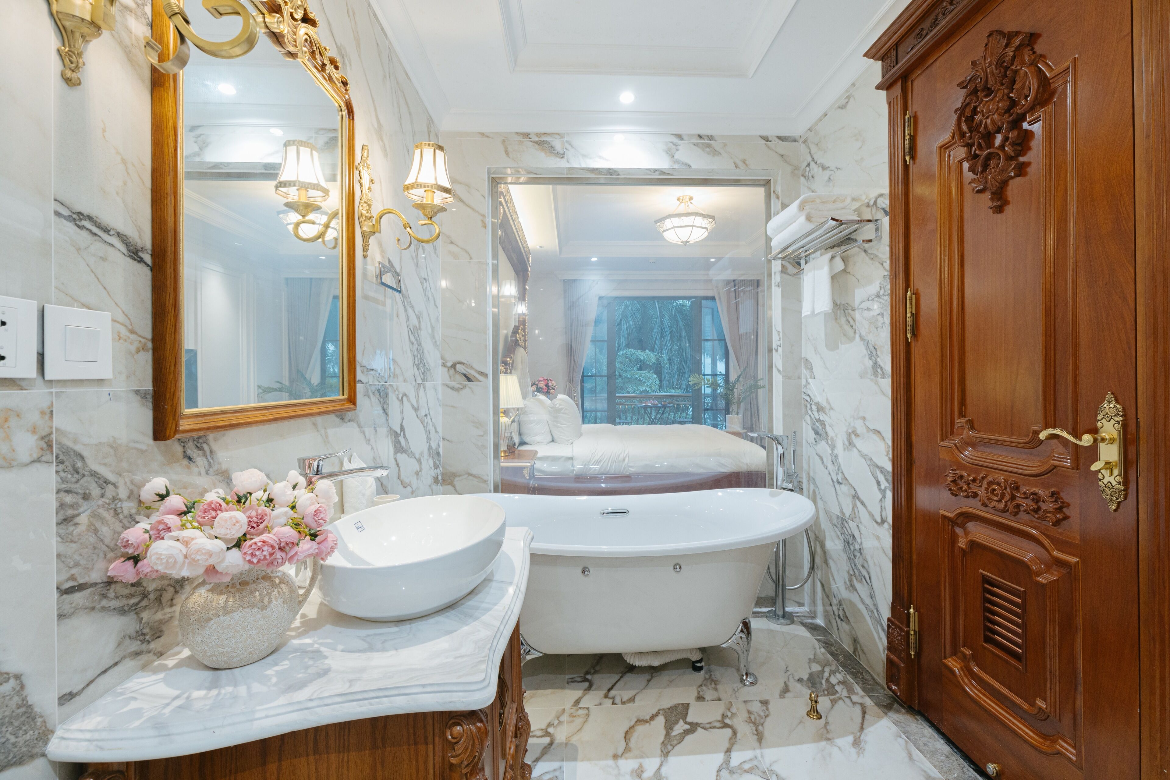A luxurious bathroom with a marble floor, a freestanding bathtub, a large mirror, and a wooden wardrobe.