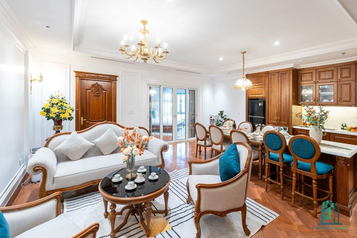 Un salon spacieux comprenant un canapé, des fauteuils, une table à manger et un coin cuisine avec des meubles en bois et un réfrigérateur.