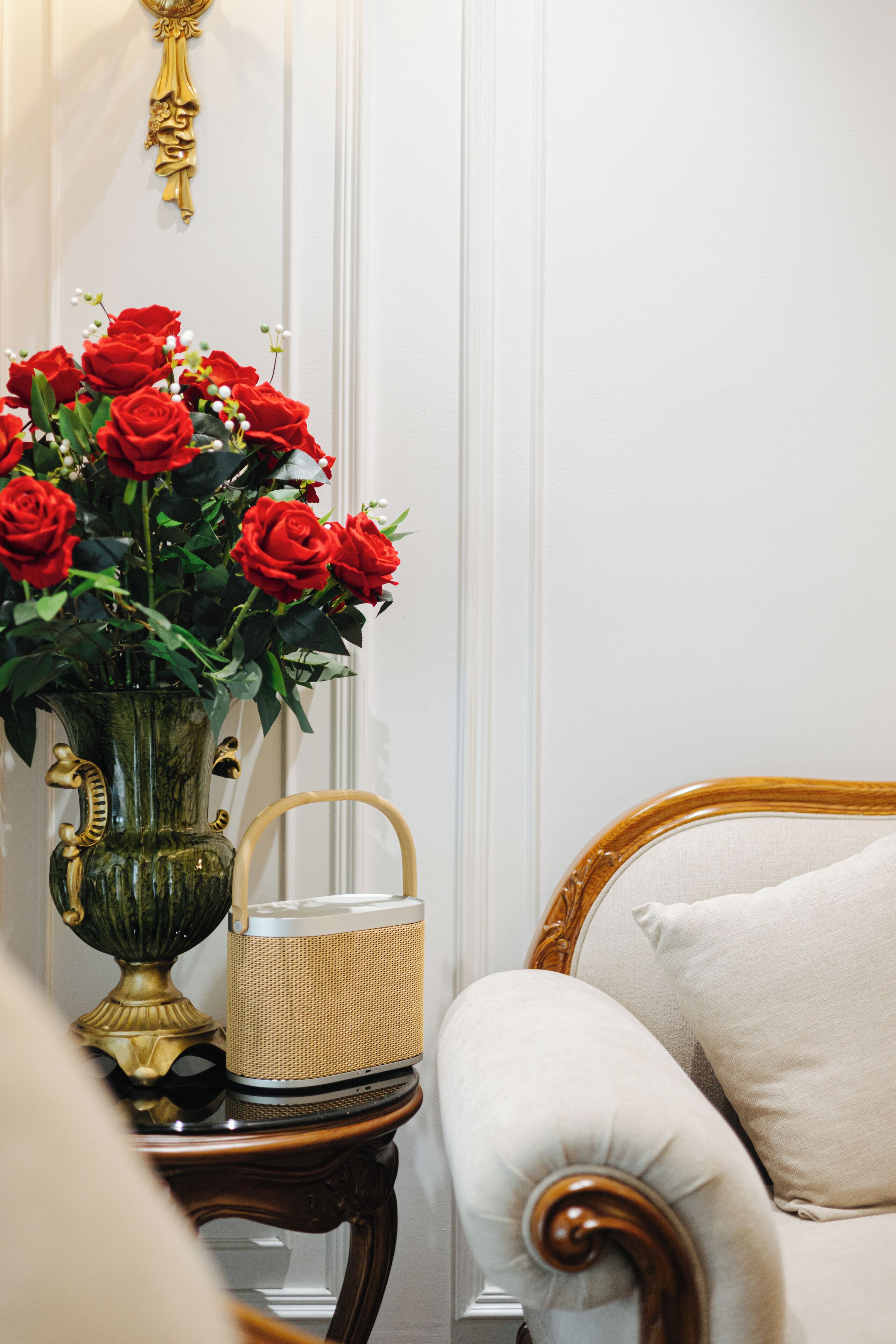 A room with a vase of red roses on a wooden side table, a wicker basket, and a white upholstered chair.