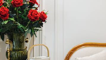 A room with a vase of red roses on a wooden side table, a wicker basket, and a white upholstered chair.
