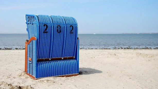 A blue beach chair with the numbers 2022 on it, placed on a sandy beach with the sea in the background. - Hier Finden Sie Ruhe und Erholung in Einem Gemütlichen und Komfortablen Friesenhaus an der Nordseeküste Ostfrieslands am Weltnaturerbe Wattenmeer (Nessmersiel)
