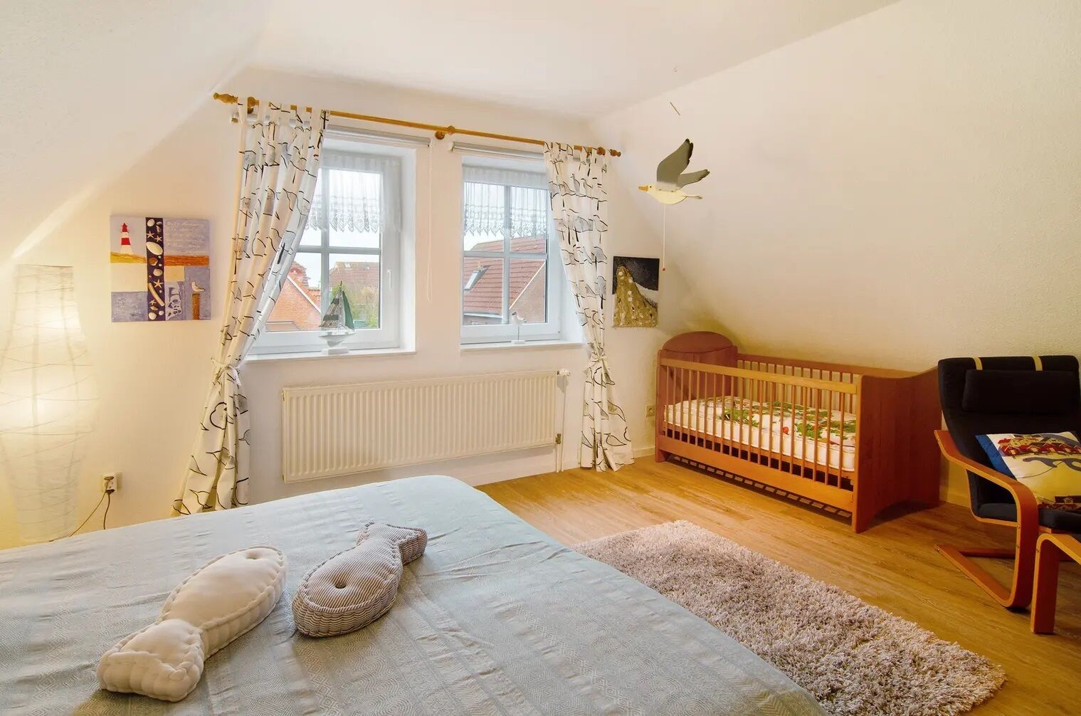 Um quarto acolhedor com uma cama, um berço, uma cadeira e uma janela com cortinas.