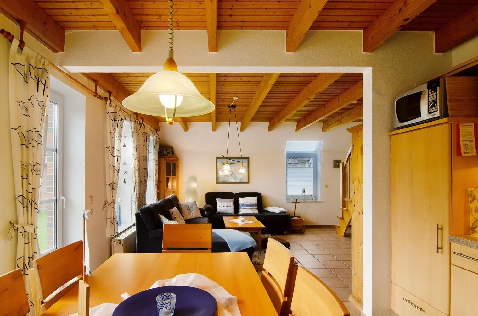 A cozy room with a wooden ceiling, a dining table with chairs, a sofa, and a television.