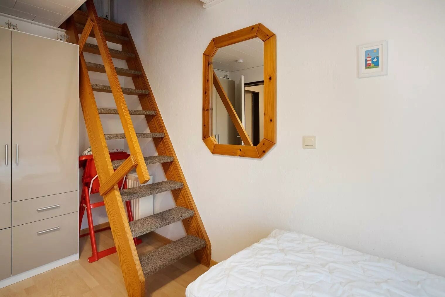 A bedroom with a wooden staircase, a bed, a wardrobe, and a mirror on the wall.