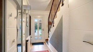 A hallway with a wooden floor, a red carpet, a white door with glass panels, and a staircase with a metal railing.