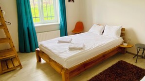 Un dormitorio con cama de madera, una mesita de noche pequeña, una silla, una ventana con cortinas y un radiador.