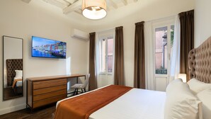 A hotel room with a bed, a wooden dresser, a desk, a chair, a large window with curtains, a wall-mounted TV, and a ceiling light fixture. - Relais del Portico (Rome)