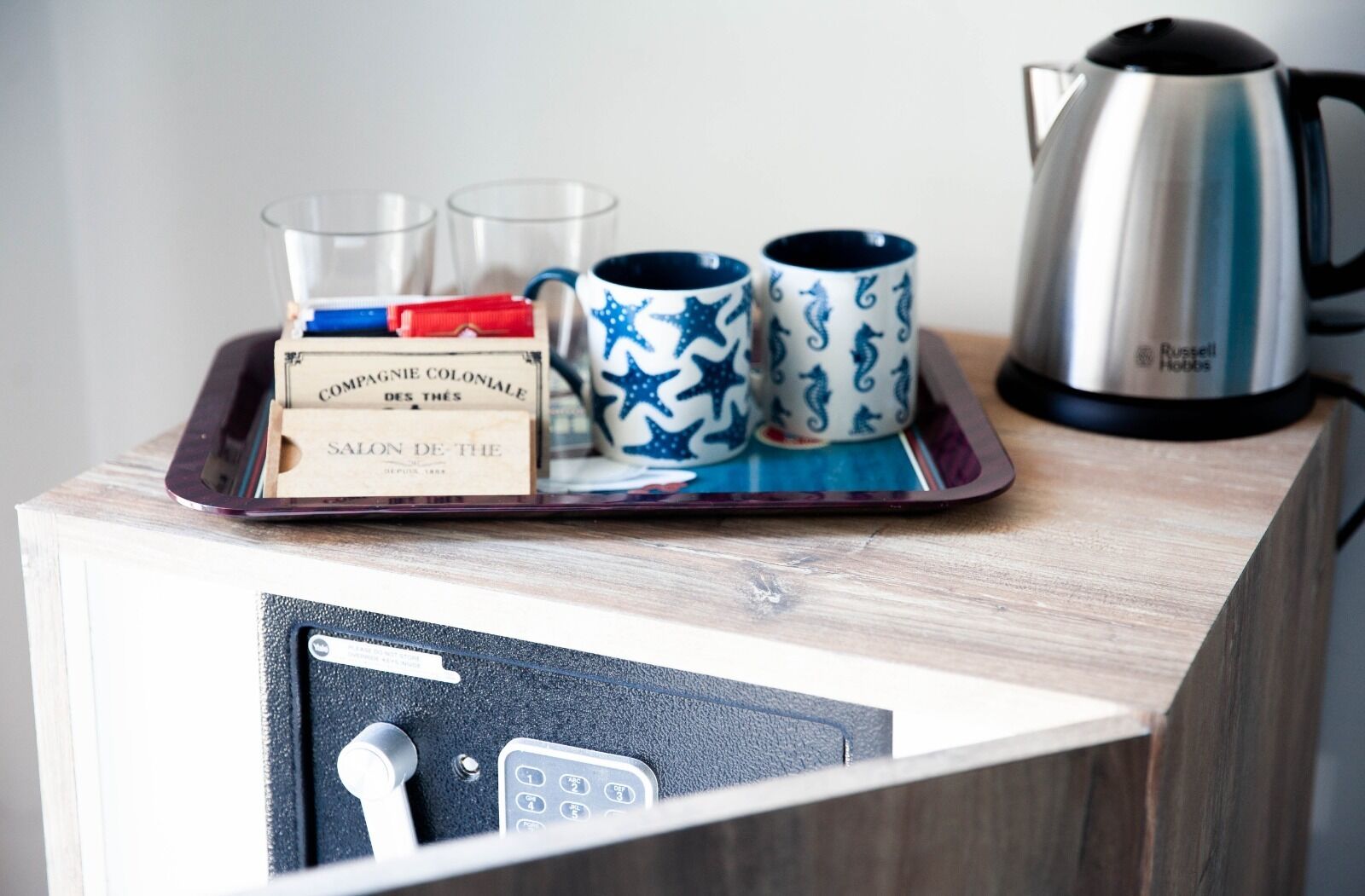 A tray with a kettle, two mugs, a box, and two glasses on a wooden surface.