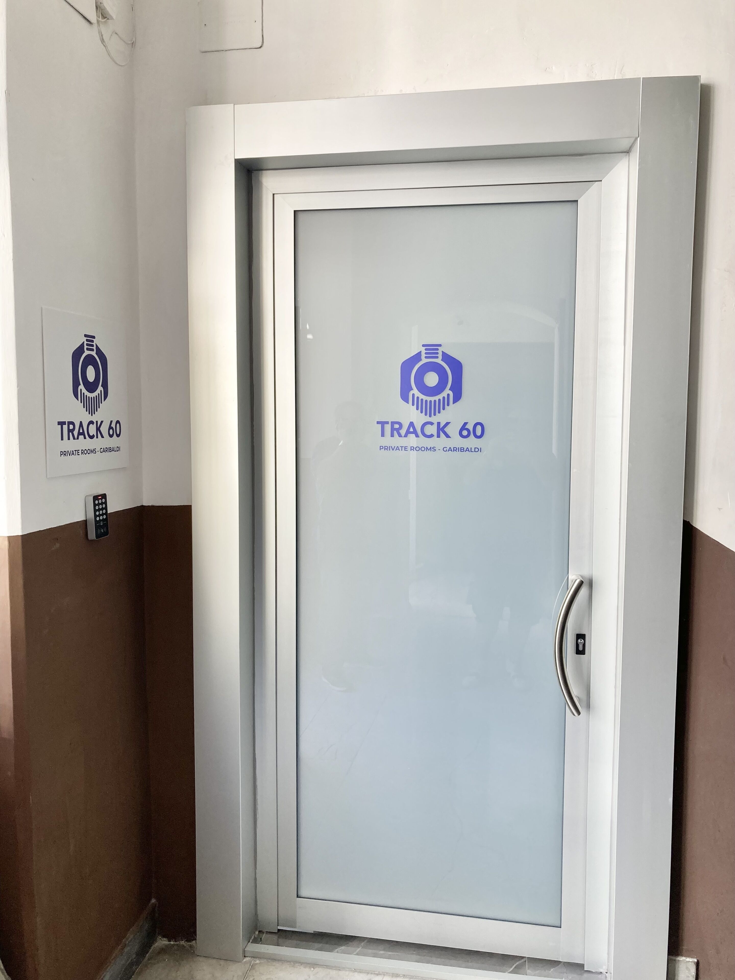 Uma porta com painel de vidro jateado e um logotipo com a inscrição 'TRACK 60 PRIVATE ROOMS - GARIBALDI'.
