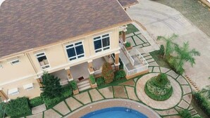 Un edificio de dos pisos con piscina, un patio cubierto y un jardín ajardinado.