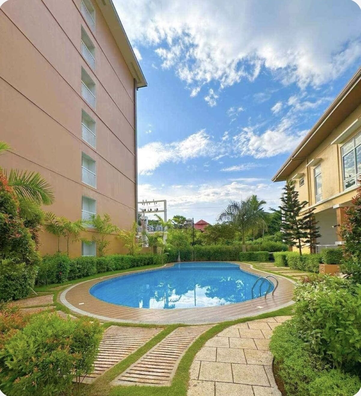 Ein von Grünpflanzen umgebener Swimmingpool, mit einem Gebäude an einer Seite und einem wolkenlosen Himmel.