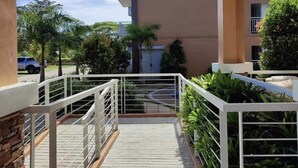 Un edificio de varios pisos con balcones, un camino de hormigón y vegetación circundante.
