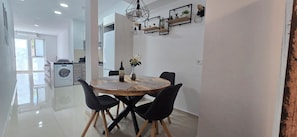 Un coin repas avec une table ronde, des chaises noires, un vase avec des fleurs et une bouteille de vin.