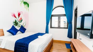 A hotel room with a bed, a TV, a window with curtains, and a view of buildings outside.