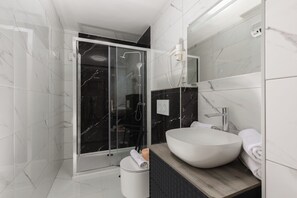 A modern bathroom with a glass-enclosed shower, a white sink, and a wooden vanity.