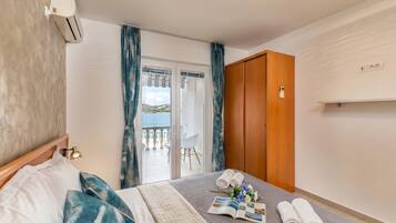 Habitación de hotel con cama, vista al balcón, puerta de madera y equipo de aire acondicionado.