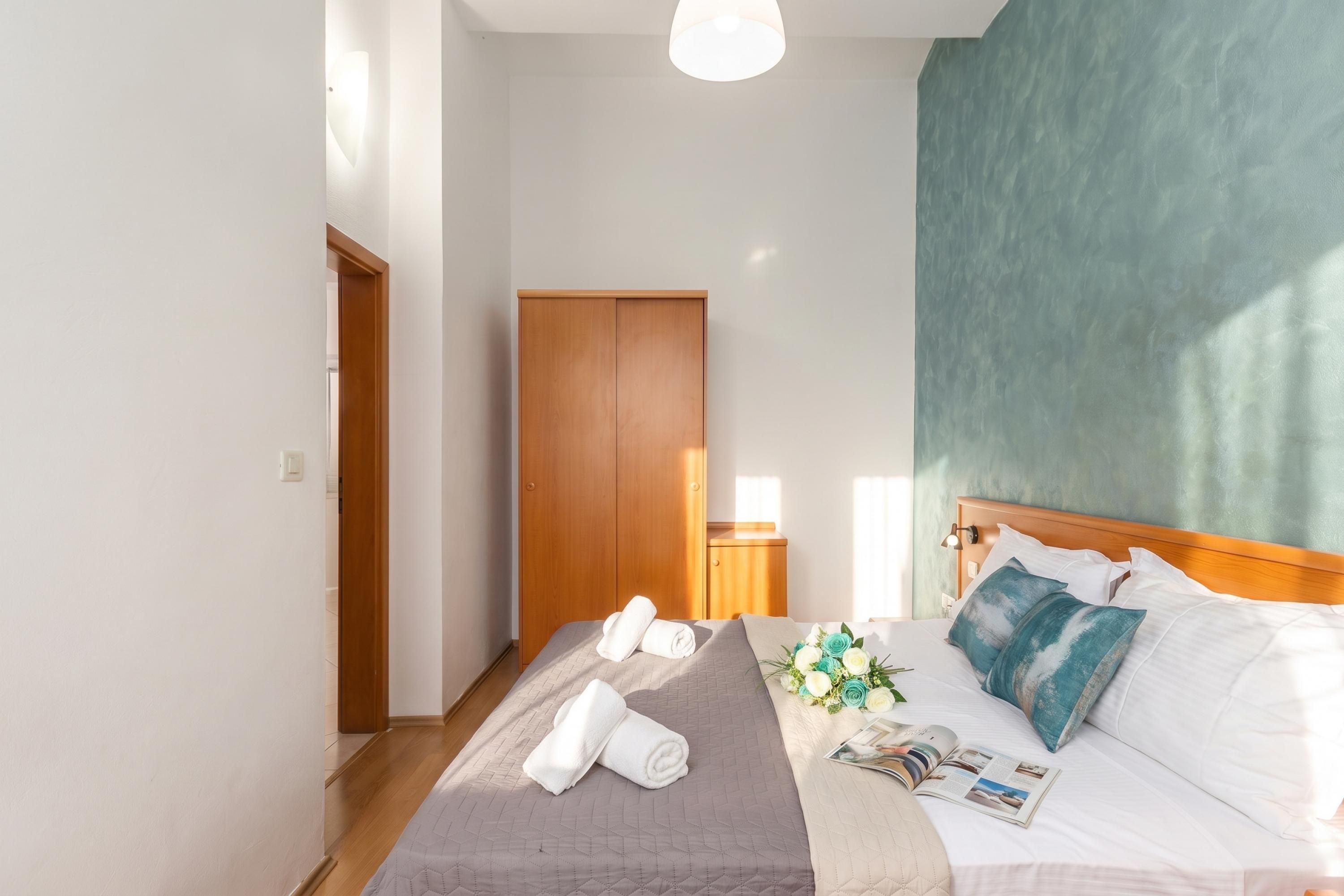 A hotel room with a bed, a wooden wardrobe, a nightstand, and a wall with a textured finish.