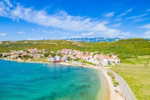 Une ville côtière avec des bâtiments qui bordent le littoral, un ciel bleu dégagé et des montagnes en arrière-plan.