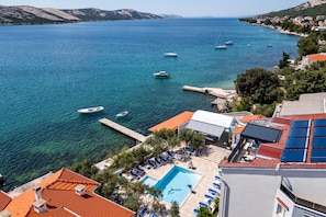 A coastal hotel with a swimming pool, lounge chairs, and boats on the water. - Family Resort Santa Maria (Novalja)