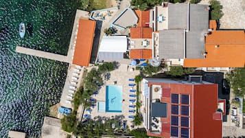 An aerial view of a coastal property with a swimming pool, multiple buildings, and a dock with a boat.