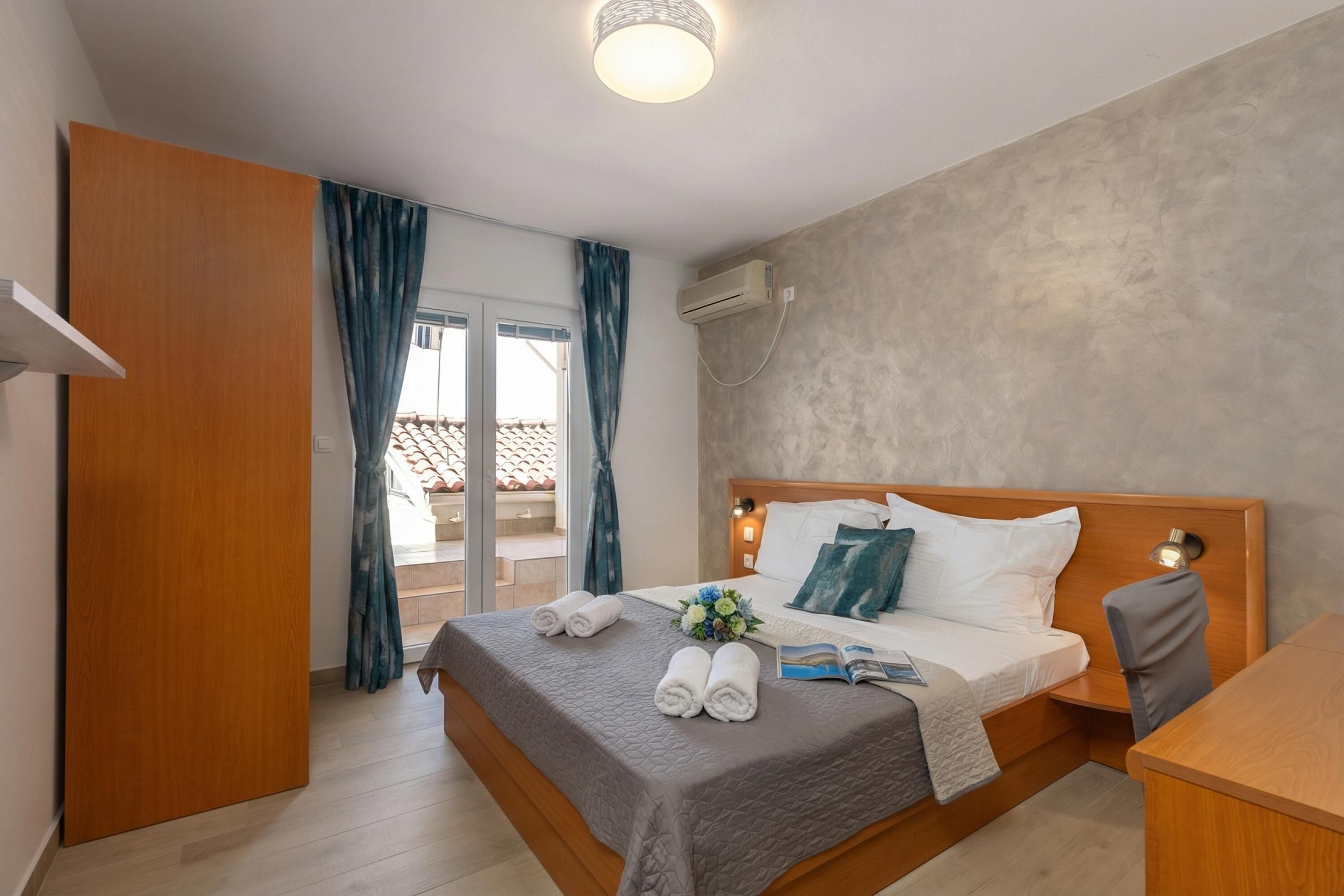 Habitación de hotel con cama, escritorio, silla, ventana con cortinas y unidad de aire acondicionado.