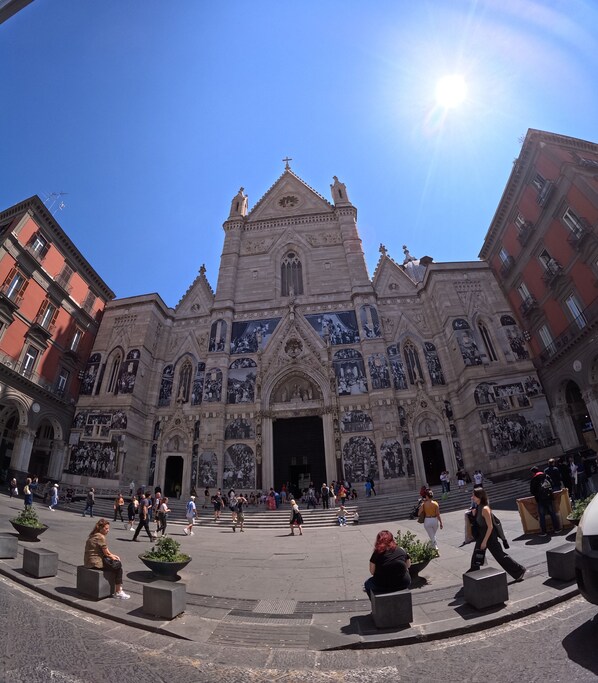 A historic building with intricate facade and large murals, surrounded by a plaza with seating areas and people. - QUEEN 20 - PRIVATE ROOMS DUOMO (Naples)