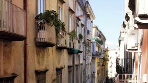 A narrow urban street with multi-story buildings, balconies with plants, and a pedestrian walkway. - QUEEN 20 - PRIVATE ROOMS DUOMO (Naples)