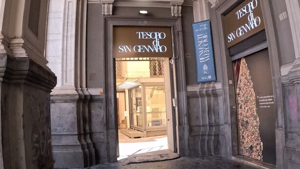 An entrance to a building with ornate architectural details, including columns and a decorative archway. There are signs for 'TESOPO DI SAN GENARO' and 'BENETTI VELOCIE'. - QUEEN 20 - PRIVATE ROOMS DUOMO (Naples)
