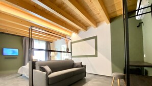 A modern living room with a grey sofa, wooden ceiling beams, a mounted TV, and a hexagonal floor pattern. - B&B ALIVA (Alcamo)