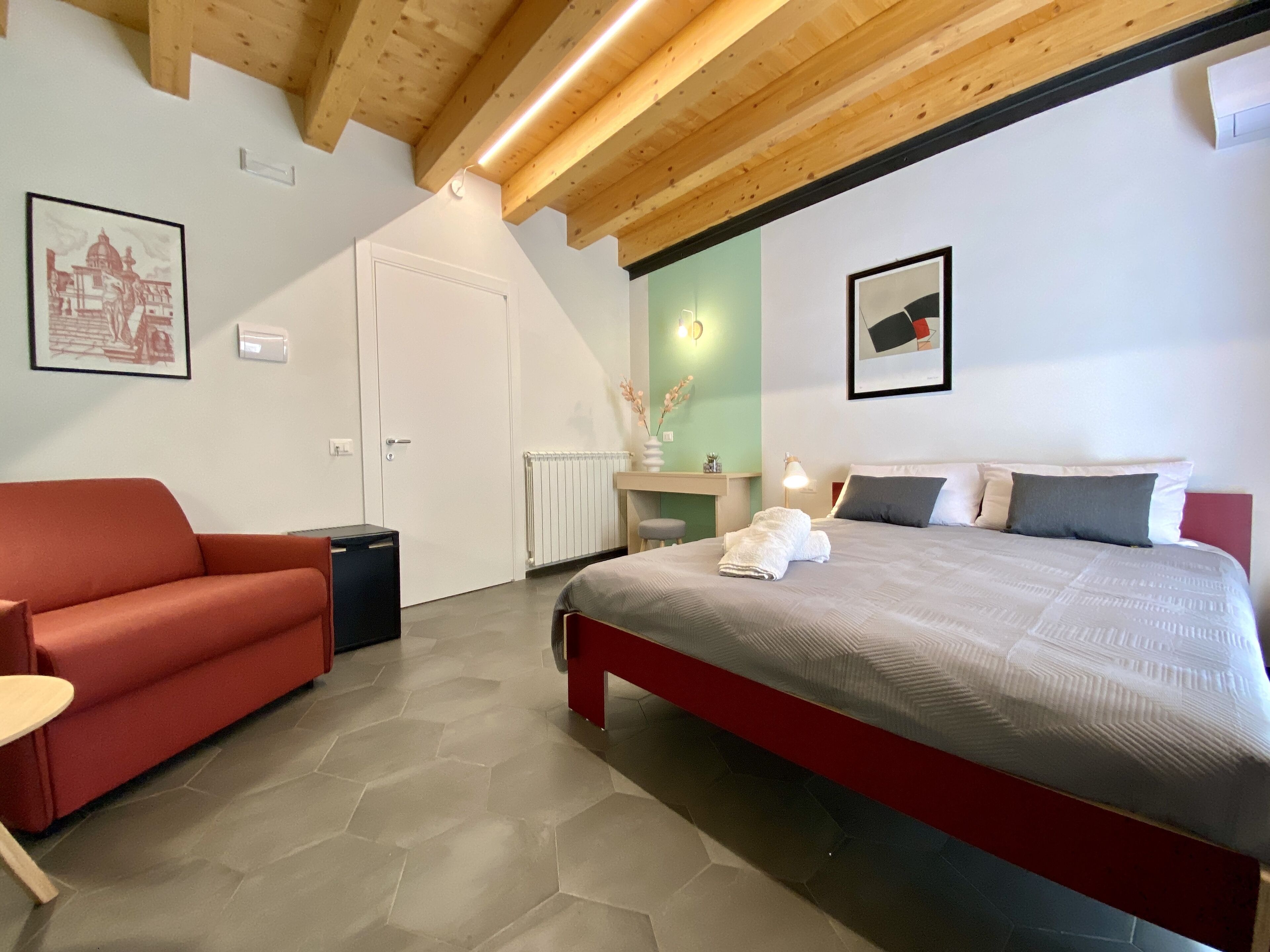 Un dormitorio con una cama, un sofá rojo, una mesita y un radiador.