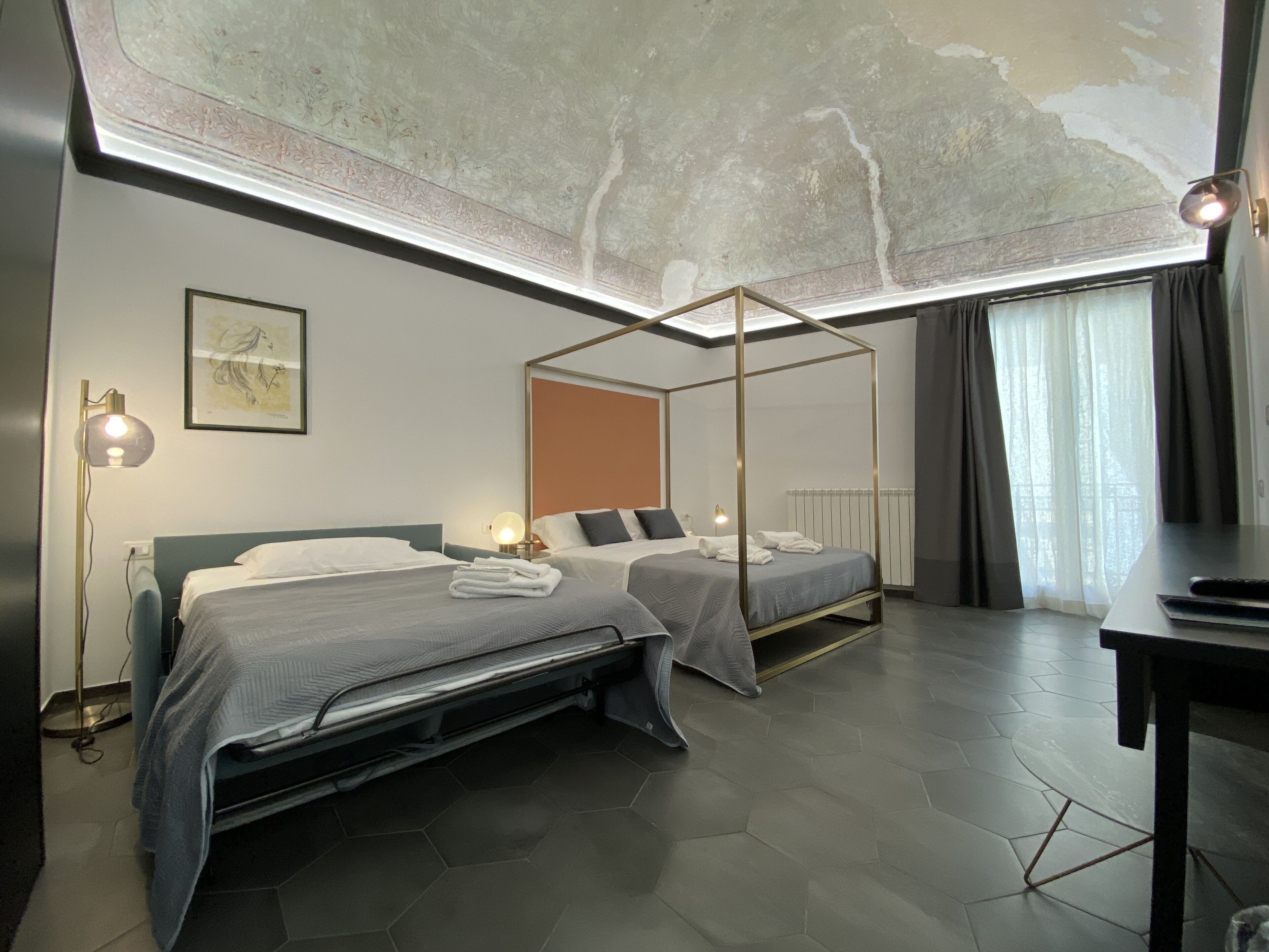 A modern hotel room with two beds, a ceiling light fixture, and a view of the city through large windows.